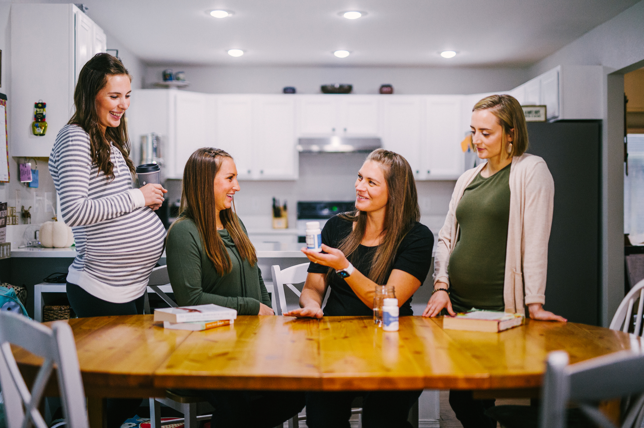 Four pregnant women sitting around a kitchen table with books and a supplement bottle of Blood Vitality.