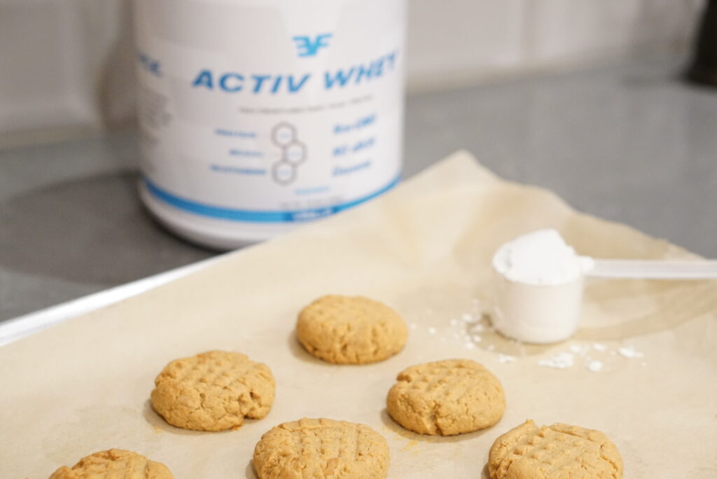 Peanut butter cookies on cookie sheet with a bottle of goat whey protein powder