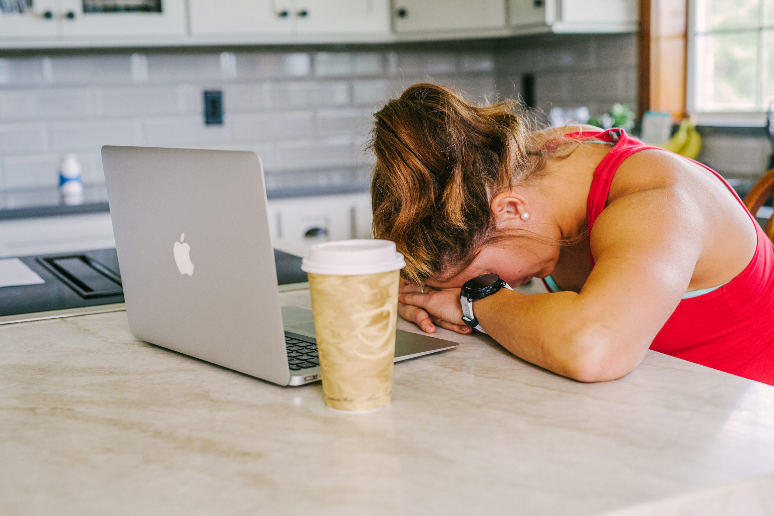 Woman sleeping at computer with a cup of coffee next to her.